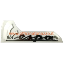 Targhetta scudo con scritta Vespa cromata e fissaggio autoadesivo, compatibile con Vespa PX 125 e PX 150 delle serie predisposte.